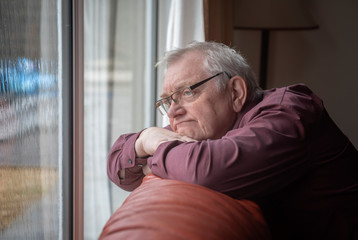 Bored man in sixties looking out the window in home 
