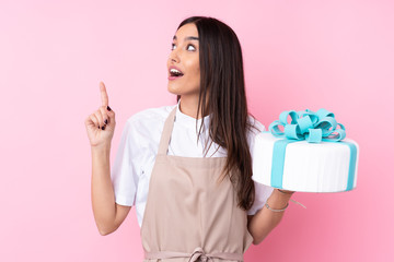 Young woman with a big cake over isolated background intending to realizes the solution while lifting a finger up