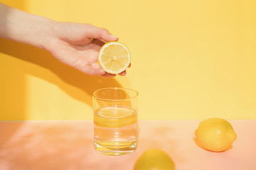 hand holding lemon. Glass with fresh lemonade on color background