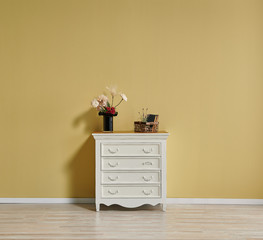 Yellow wall background in the room, white cabinet, chair and frame decor.