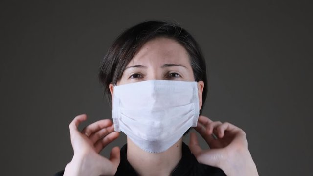 Portrait of a Caucasian woman wearing and taking off a white medical mask. Protection against contagious disease, coronavirus