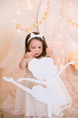 Cute little girl in a white princess dress with a bow on her hair plays with wooden ballerinas...