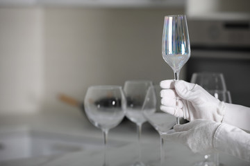 Person in white gloves checking cleanliness of glass indoors, closeup. Space for text