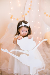 Cute little girl in a white princess dress with a bow on her hair plays with wooden ballerinas...