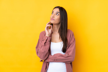 Young brunette woman over isolated yellow background thinking an idea while looking up