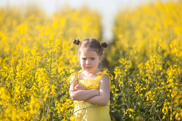 Cute girl in a yellow dress having fun in the field of flowering rape