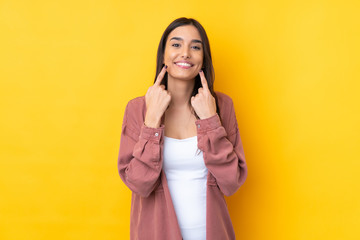 Young brunette woman over isolated yellow background smiling with a happy and pleasant expression