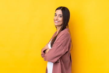 Young brunette woman over isolated yellow background with arms crossed and looking forward