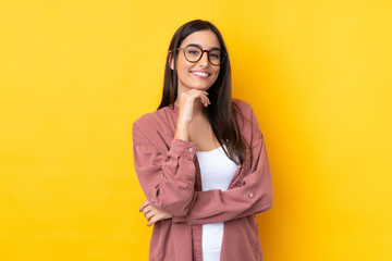 Young brunette woman over isolated yellow background with glasses and smiling - obrazy, fototapety, plakaty