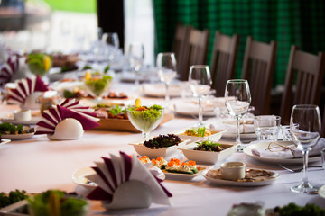 Glasses, flowers, fork, knife served for dinner in restaurant with cozy interior