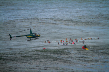 Big wave surfers waiting in the lineup with helicopter above