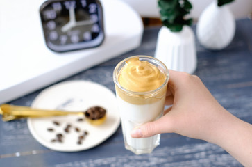 Fototapeta na wymiar Iced frothy Dalgona Coffee, a trendy fluffy creamy whipped coffee. Korean drink latte espresso with coffee foam. hand holding cup with instant coffee.