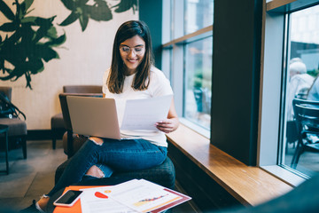 Successful female digital nomad enjoying working remotely checking finance reports from project earning in coworking space, happy woman student satisfied with education course using technology