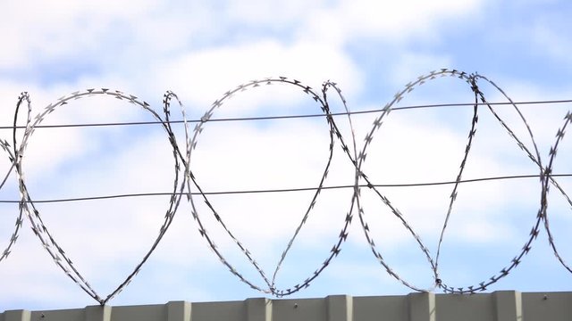 Barbed wire, razor wire on top of steel fence on blue sky background. Forbidden territory or protected area, military facility, prison or secret territory.