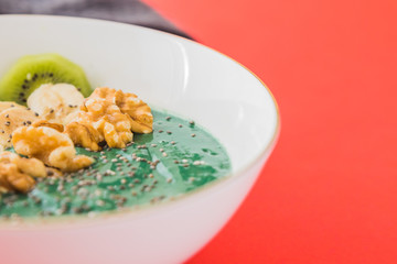 spirulina smoothie bowl with banana, walnuts, kiwi and chia seeds on red background