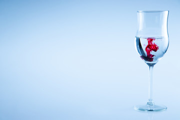 Glass with water and drop of red ink. Half full glass wine isolated.