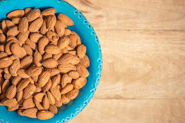 Shelled sicilan almonds on blue bowl, view from above, copy space, light brown blurred wooden background