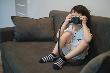 Beautiful smiling child (kid, boy) - photographer holding a instant camera intdoors