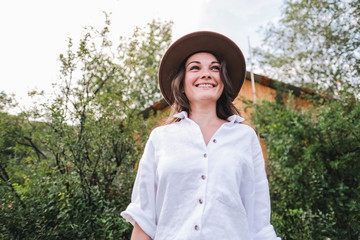 Attractive brunette in a hat and white shirt is enjoying nature in the mountains. Beautiful young woman in a shirt and jeans walks along the beautiful landscape