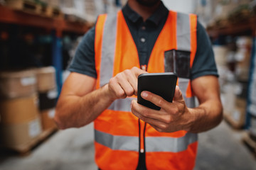 Closeup of man hands using mobile phone while in warehouse in uniform - Powered by Adobe