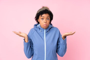 African american woman with winter hat over isolated pink background having doubts with confuse...