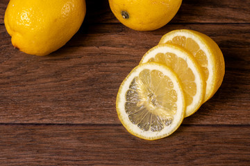 Yellow juicy sour lemon, slices of chopped lemon on a brown wooden background. Vitamin C in citrus...