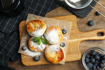 Delicious cottage cheese pancakes with blueberries and sugar powder on wooden table, flat lay