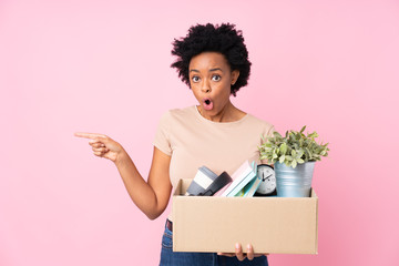 African american woman making a move while picking up a box full of things surprised and pointing...