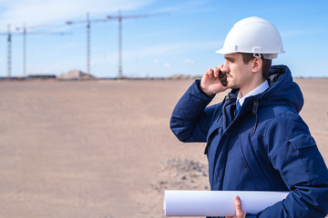 a civil engineer in a white helmet is talking on the phone in the background of construction.