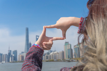 Asian girl with dyed hair raises her hands and make the finger frame with the background of the Shanghai Lujiazui Cityscape and sky scrappers skyline in the sunny day