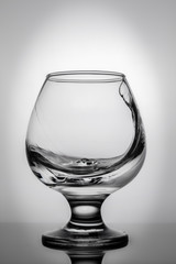 Glass with a clear liquid on a white background. The liquid hits the glass wall