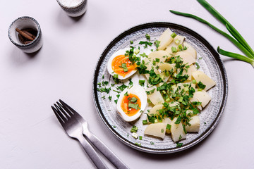 Boiled potatoes with herbs and soft-boiled eggs in a plate on grey concrete background. Selective focus