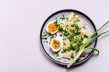 Boiled potatoes with herbs and soft-boiled eggs in a plate on grey concrete background. Selective focus