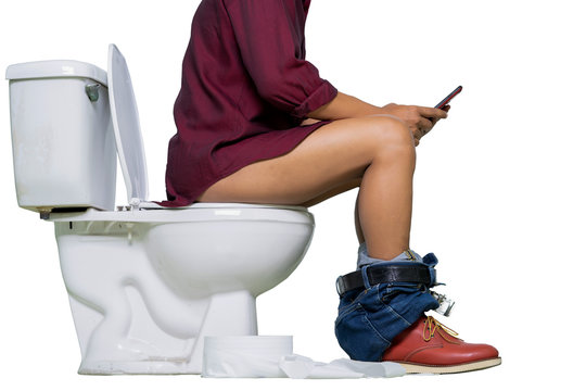 Man wearing jeans and shoes using phone while sitting on a toilet isolate on white background