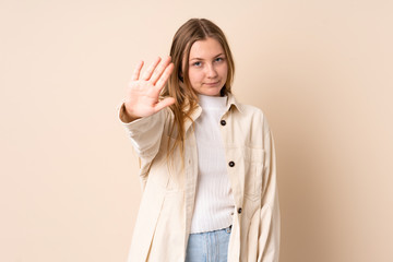 Teenager Ukrainian girl isolated on beige background making stop gesture and disappointed