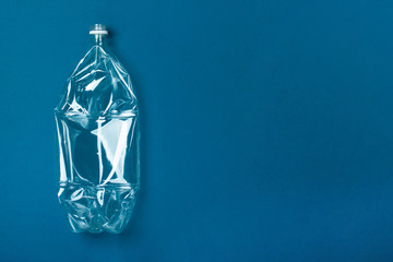 One used plastic bottle on a blue background. The concept of pollution of the planet and the oceans with plastic waste. Copy space.