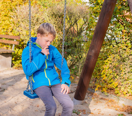 Kind sitzt nachdenklich auf einem Spielplatz auf einer Schaukel