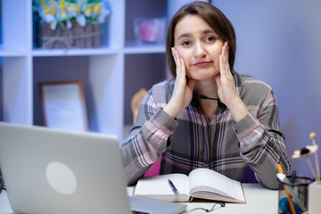 Cute girl looking and overwhelmed sitting at the desk at home doing homework. Stress emotions...