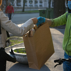 Delivery man give the online express order to receiver woman during the quarantine. Young beautiful woman receives her order from cheerful courier in medical mask and gloves.Food delivery concept.
