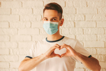 Happy doctor in protective mask on face gesturing heart symbol by hands. Young man in medical face...