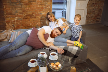 Mother, father and son at home having fun, comfort and cozy, love concept. Looks happy, cheerful and joyful. Beautiful caucasian family. Spending time together, playing, watching cinema, lying on sofa