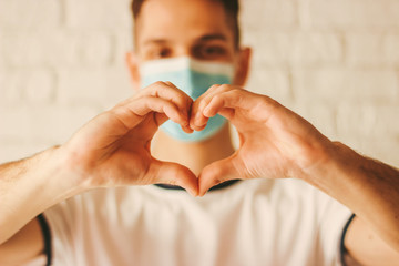 Young man in medical face mask gesturing love shape symbol by hands. Happy doctor in protective...