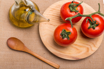 glass container with olive oil next to some red tomatoes on a wooden board, on a brown background, seen from above