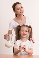 Mom pours daughter a milk in a glass on a white background