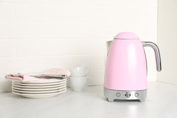 Modern electric kettle and dishes on counter in kitchen