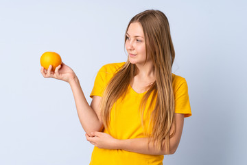 Teenager Ukrainian girl isolated on blue background holding an orange