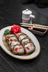 fried warm sushi with red caviar of fish rice wasabi ginger green on a black wooden background