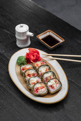 fried warm sushi with red caviar of fish rice wasabi ginger green on a black wooden background
