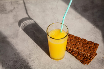 A glass of fresh orange juice on a gray concrete background. Drink in the sun with a beautiful shadow