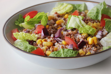 Buckwheat porridge with vegetables, onion, lettuce, tomato, horn in a bowl on white background